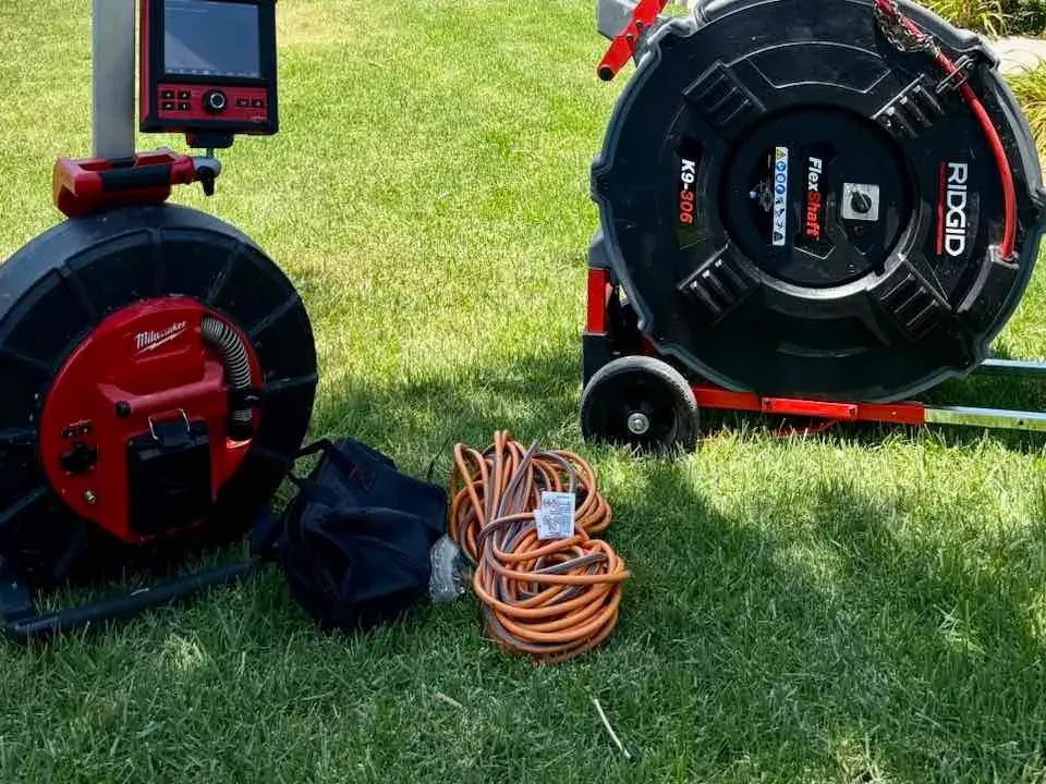 A sewer inspection camera reel and a drain machine staged on a front lawn, with the camera monitor set up beside them